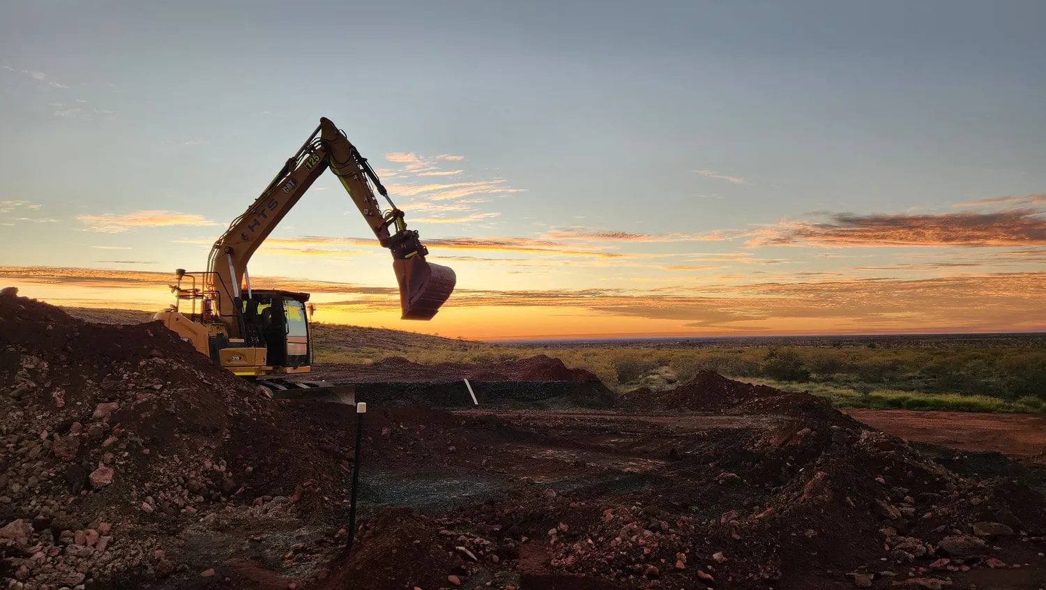Excavator silhouetted against a sunset on a remote worksite
