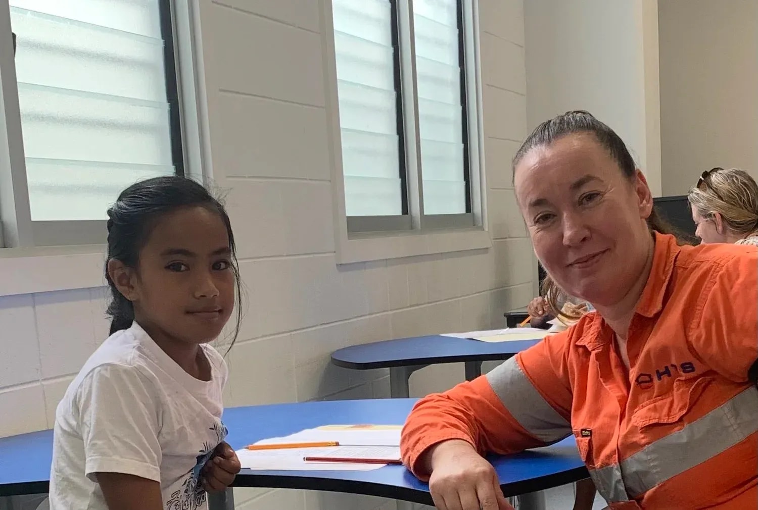 HTS Constructions worker sitting with a local student at a classroom desk