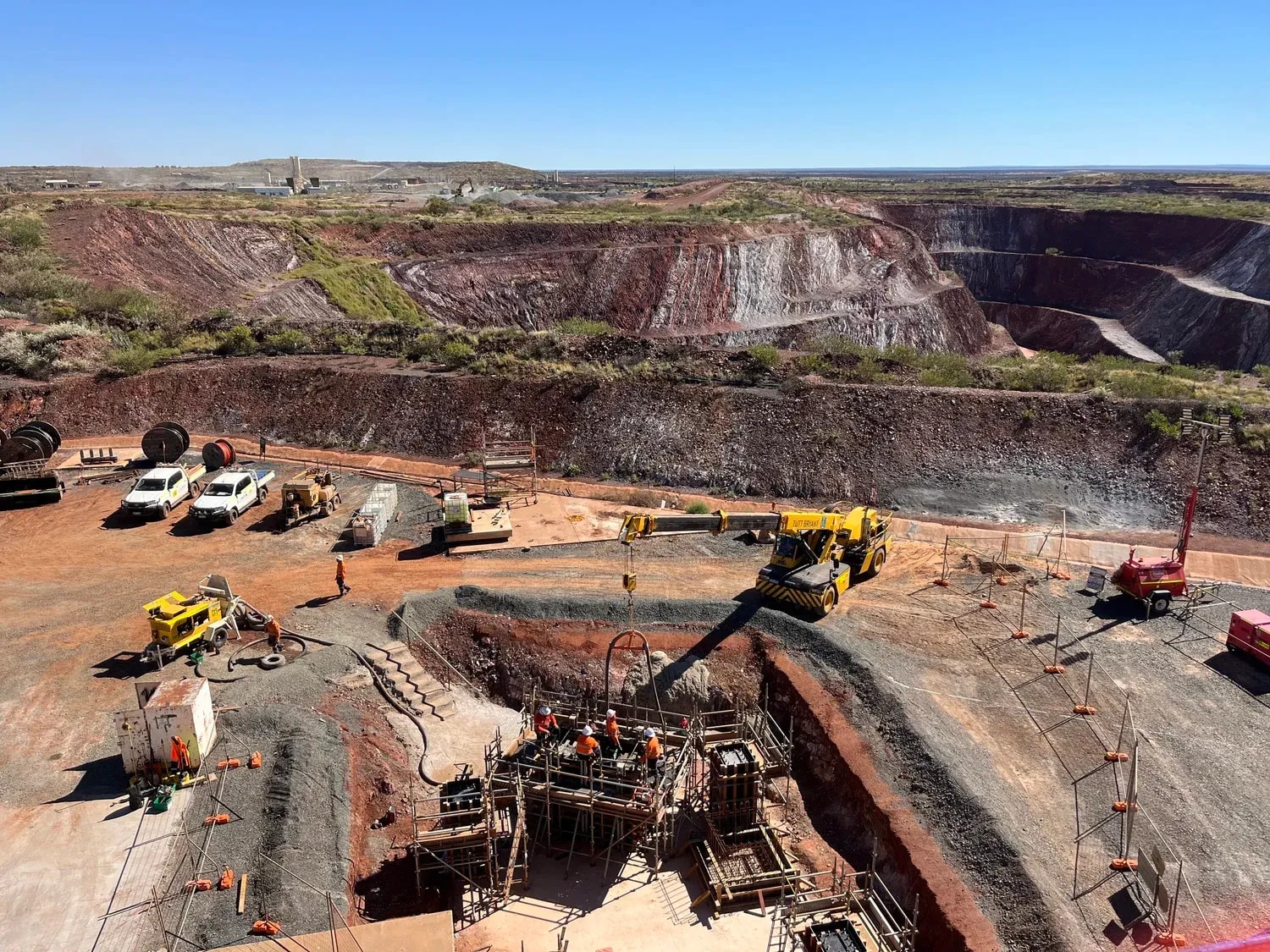 Aerial view of a crane and formwork crew working beside an open-pit mine